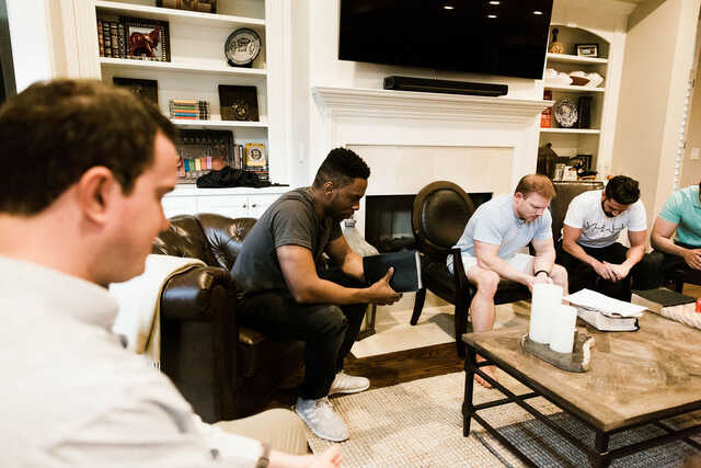 group of men praying together in a living room