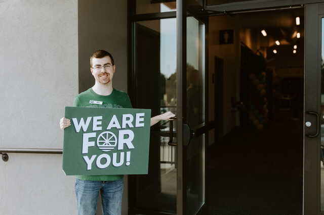 guest services volunteer greeting at the entrance with a we are for you sign