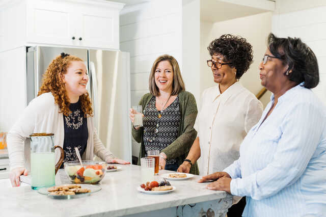 diverse group of women standing around a kitchen island having a lighthearted conversation